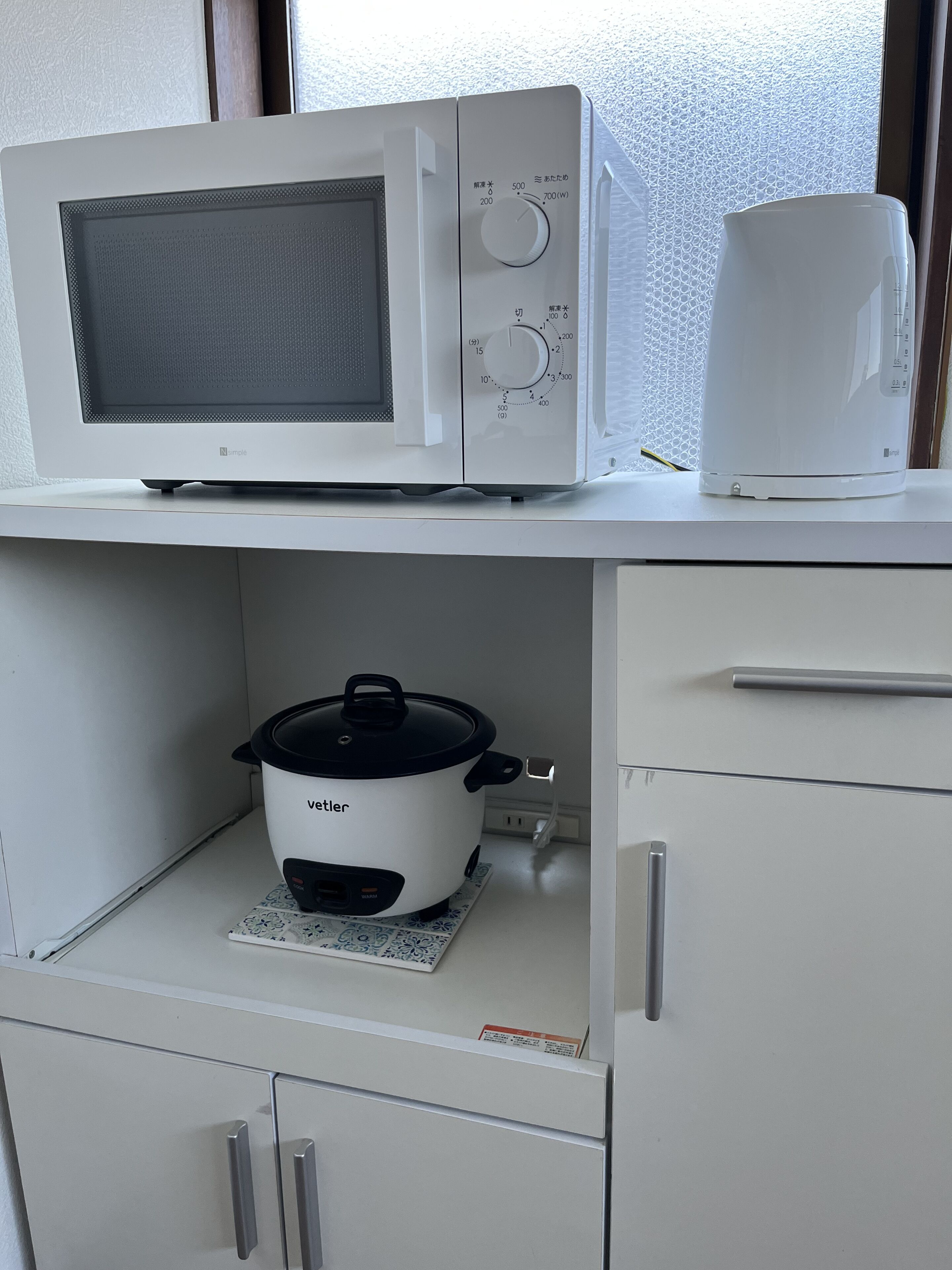 A kitchen with a microwave, a kettle, and a slow cooker on the countertop.