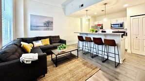 Un salon moderne avec un canapé foncé, une table basse et un coin bar équipé de tabourets.