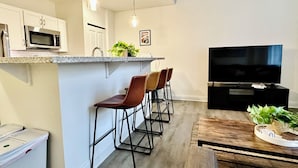 Une cuisine moderne équipée d’un four à micro-ondes, de tabourets de bar, d’une télévision et d’un coin repas avec une table en bois.