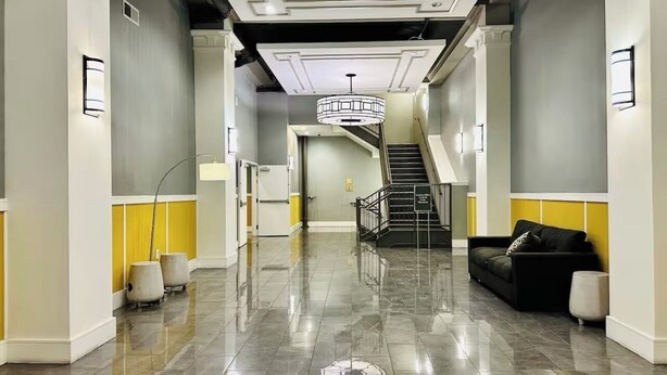 Un hall d’entrée spacieux avec un sol en marbre, un escalier et un canapé noir.