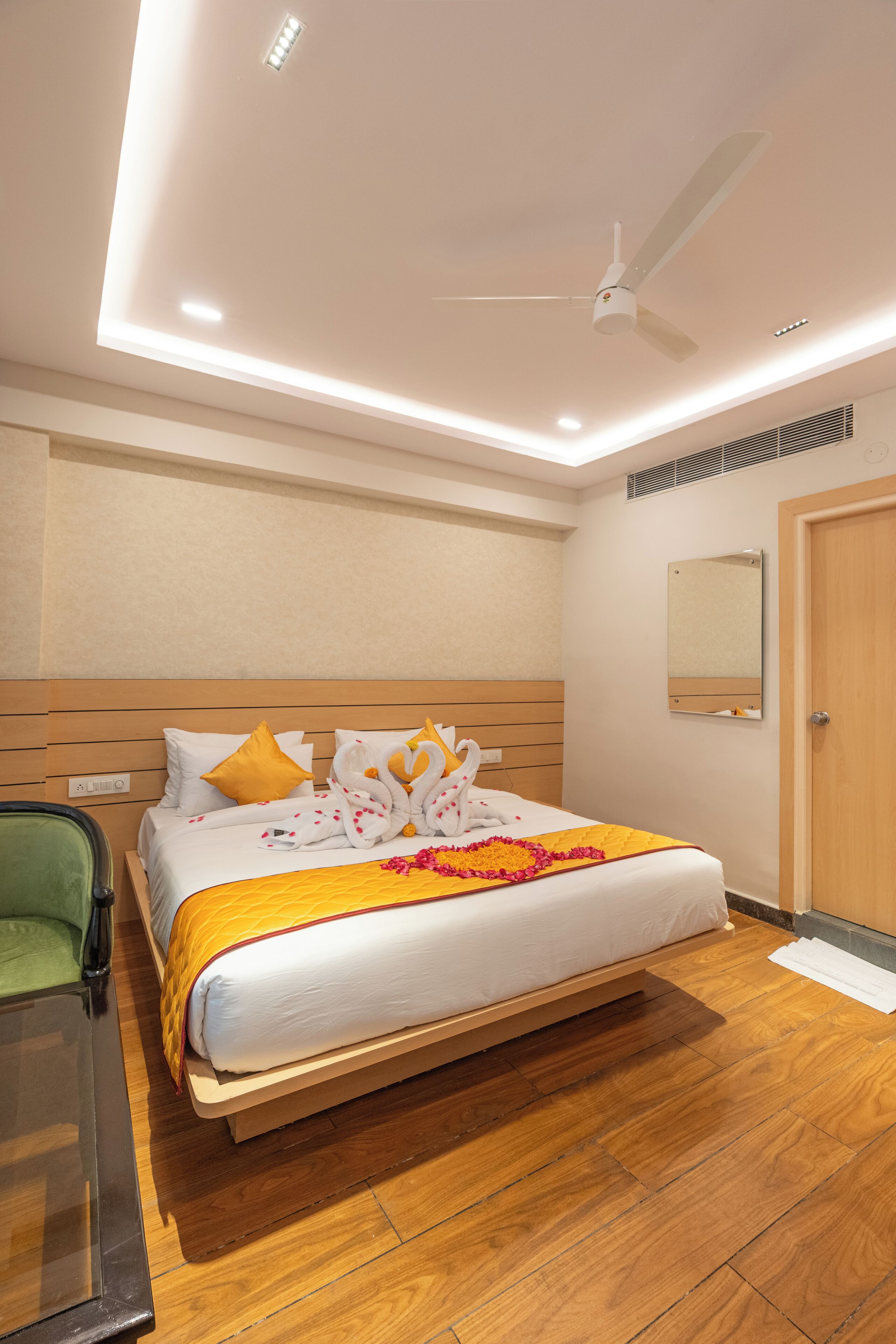 A hotel room with a wooden bed, a ceiling fan, a mirror, and a wooden floor.