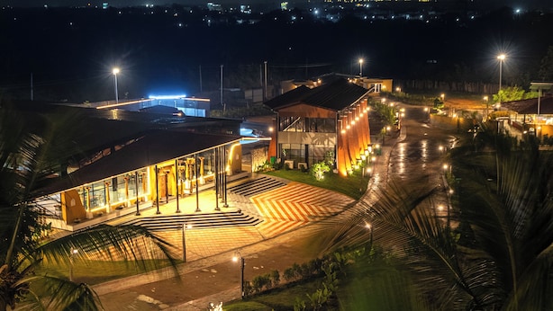 Un edificio moderno con techo curvo, una entrada bien iluminada y un área pavimentada con escalones que conducen a la entrada.