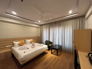A hotel room with a bed, a desk, a chair, a ceiling fan, and a large window with curtains.