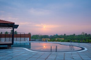An outdoor swimming pool with a curved design, surrounded by a tiled deck and a covered seating area.
