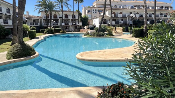 A swimming pool surrounded by palm trees and a multi-story building with balconies. - Duplex apartament Bahia Azul on the beachfront for 4 persons (Dénia)