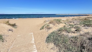 A sandy beach with a wooden boardwalk leading to the water, surrounded by sparse vegetation. - Duplex apartament Bahia Azul on the beachfront for 4 persons (Dénia)