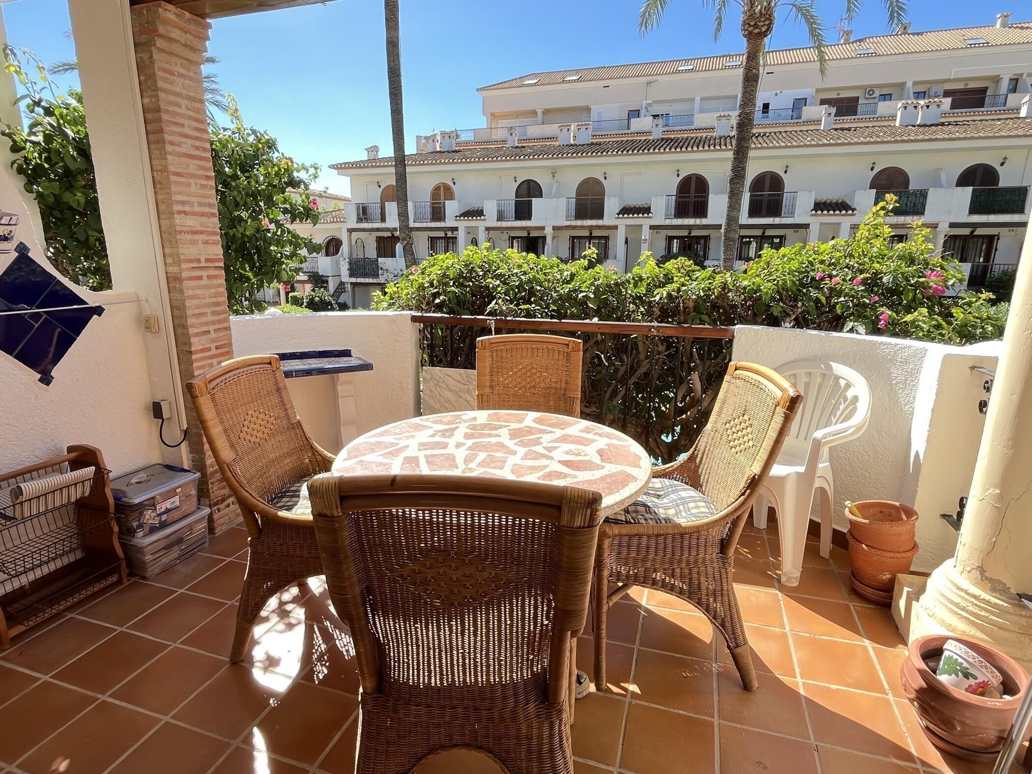A terrace with wicker furniture, a tiled floor, and a view of a building with arches and balconies.
