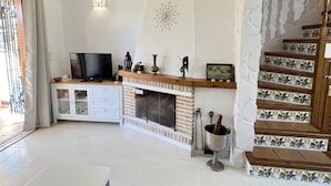 A living room with a fireplace, a TV, and a staircase with decorative tiles. - Duplex apartament Bahia Azul on the beachfront for 4 persons (Dénia)