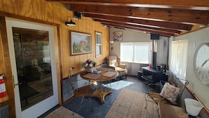 Ein gemütliches Blockhauss-Interieur mit Holzbalkendecke, Kamin, Esstisch mit Stühlen und einem großen Fenster.