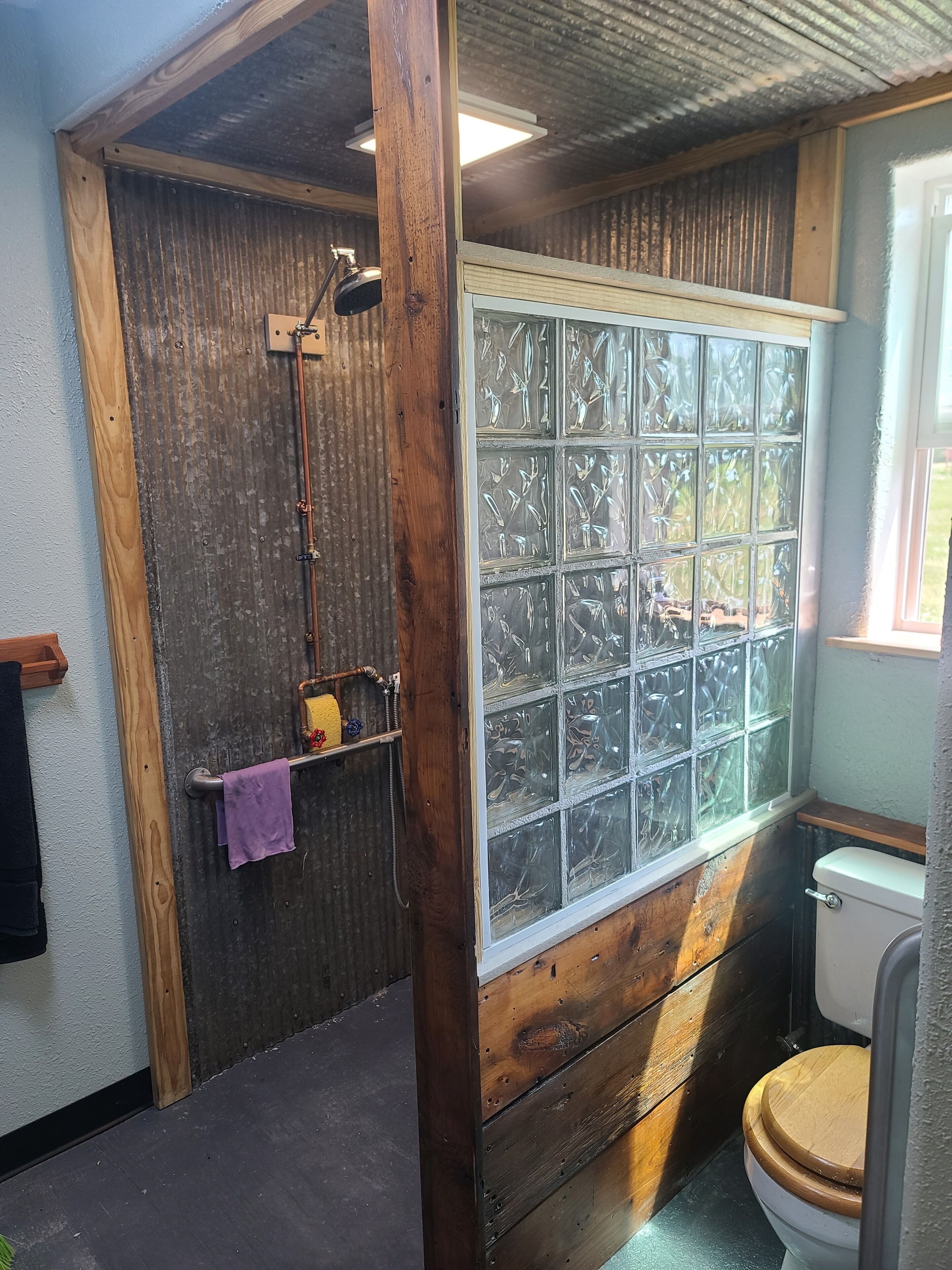 Un baño rústico con puerta de madera, ventana con vidrio esmerilado, inodoro y zona de ducha.