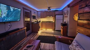 Un espace de vie compact comprenant un coin cuisine, un téléviseur à écran plat, un plancher en bois et un ventilateur de plafond.