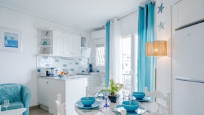 A modern kitchen with white cabinets, a dining area with blue chairs and a table, and a view of the city through large windows. - Essence by Interhome (Dénia)