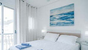 A hotel room with a bed, two pillows, a nightstand, a lamp, and a painting on the wall. - Essence by Interhome (Dénia)