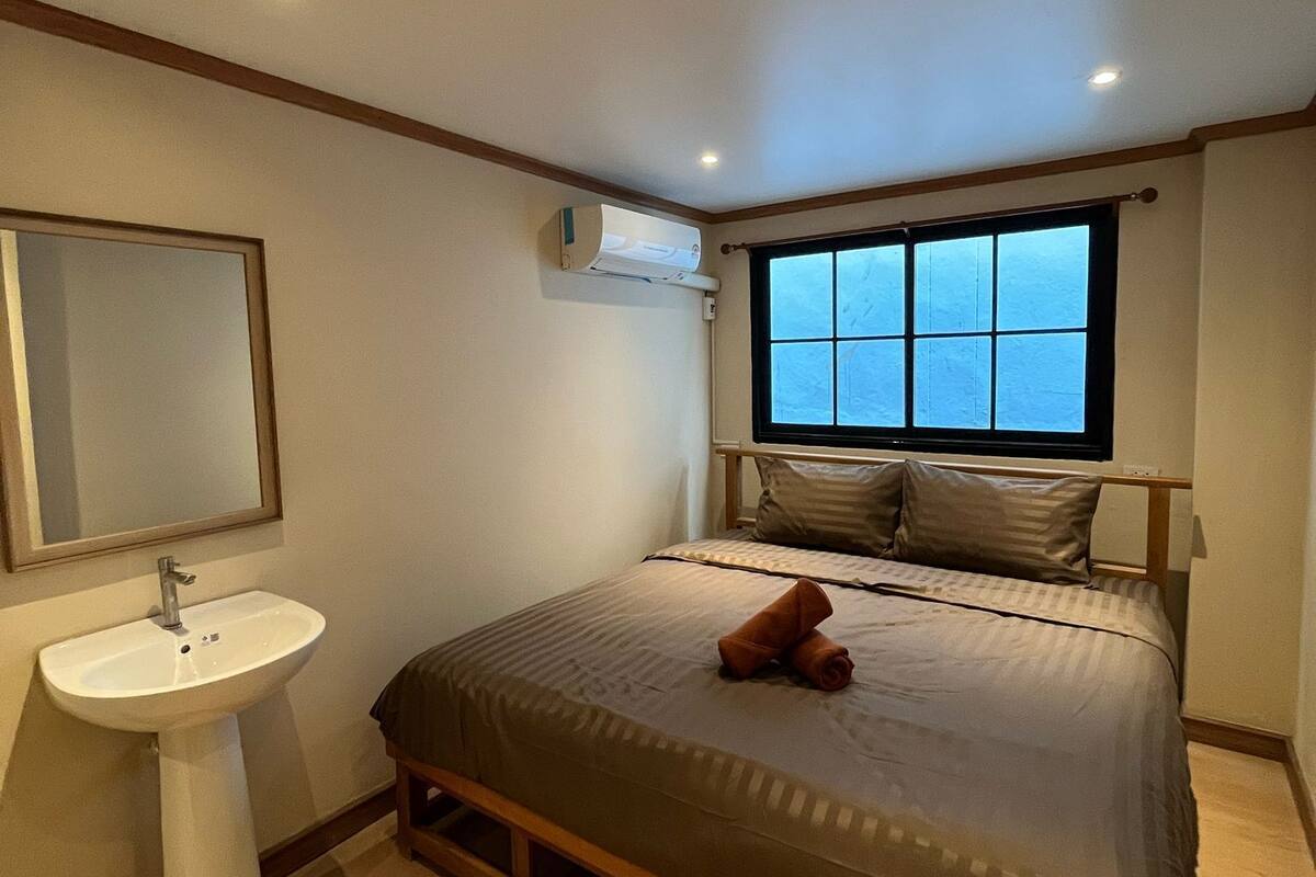 Ein Schlafzimmer mit Bett, Nachttisch, Spiegel, Fenster und Klimaanlage.