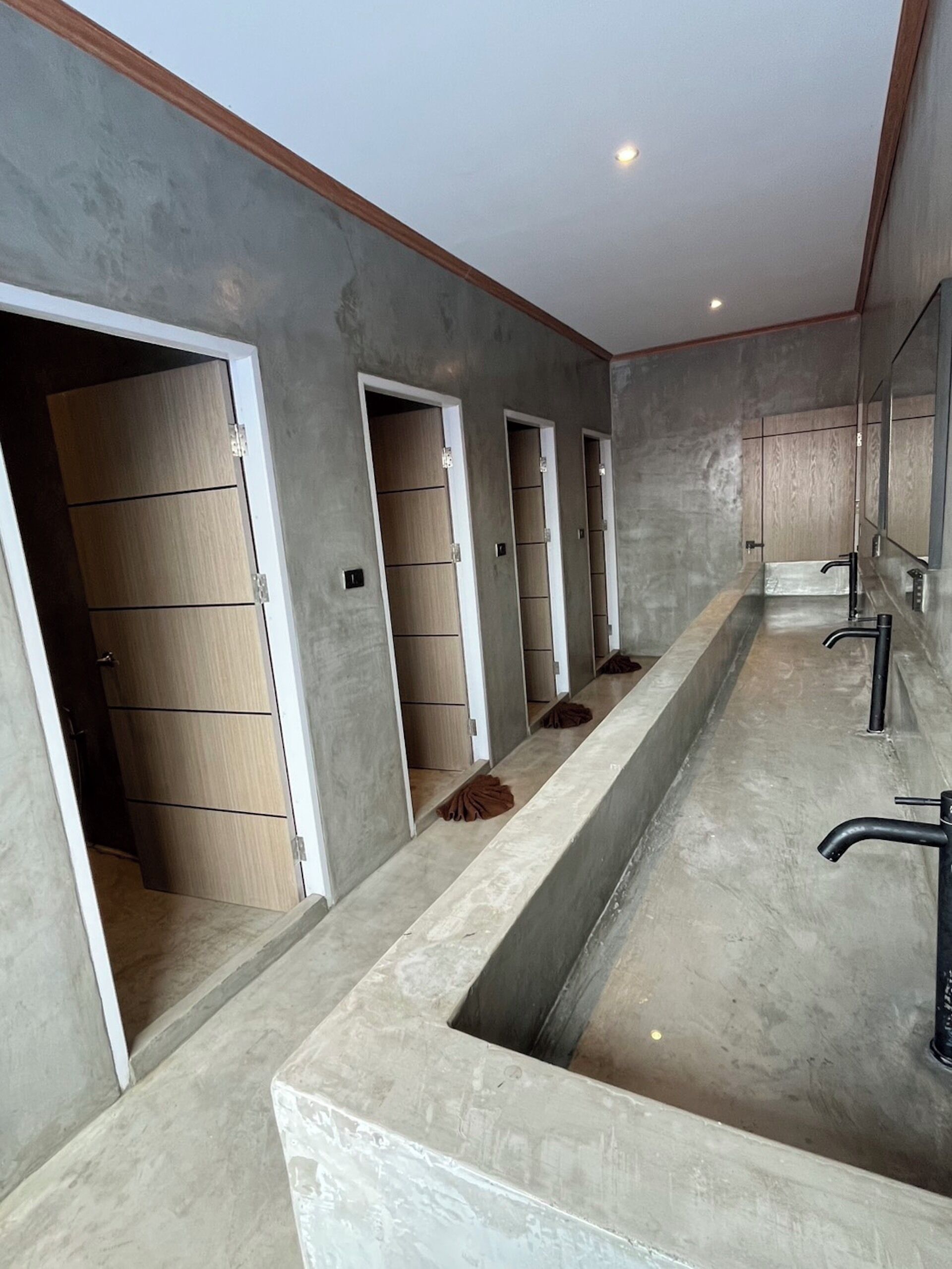 Un baño moderno con un lavamanos largo y central, y varias cabinas de ducha.