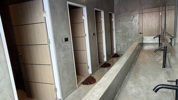 Un baño moderno con un lavamanos largo y central, y varias cabinas de ducha.