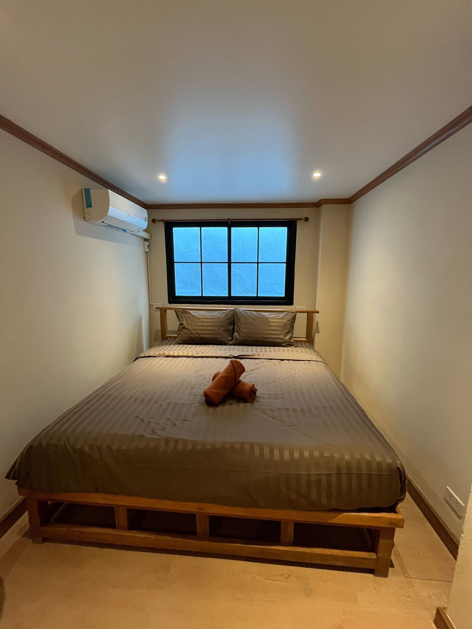 Un dormitorio con cama, almohadas, ventana y equipo de aire acondicionado.