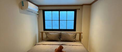 Un dormitorio con cama, almohadas, ventana y equipo de aire acondicionado.