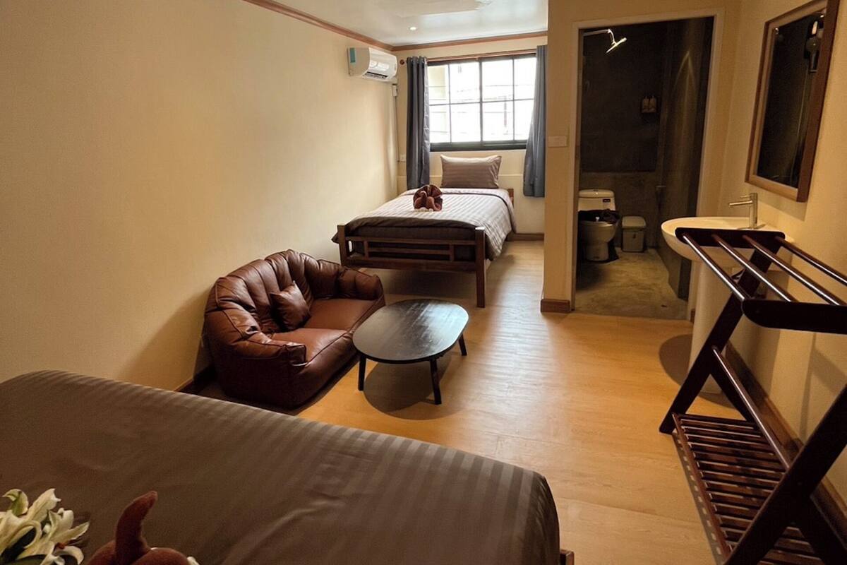 Ein Hotelzimmer mit einem Bett, einem Schlafsofa, einem kleinen Tisch, einem Schreibtisch mit Spiegel und einem Fenster mit Vorhängen.