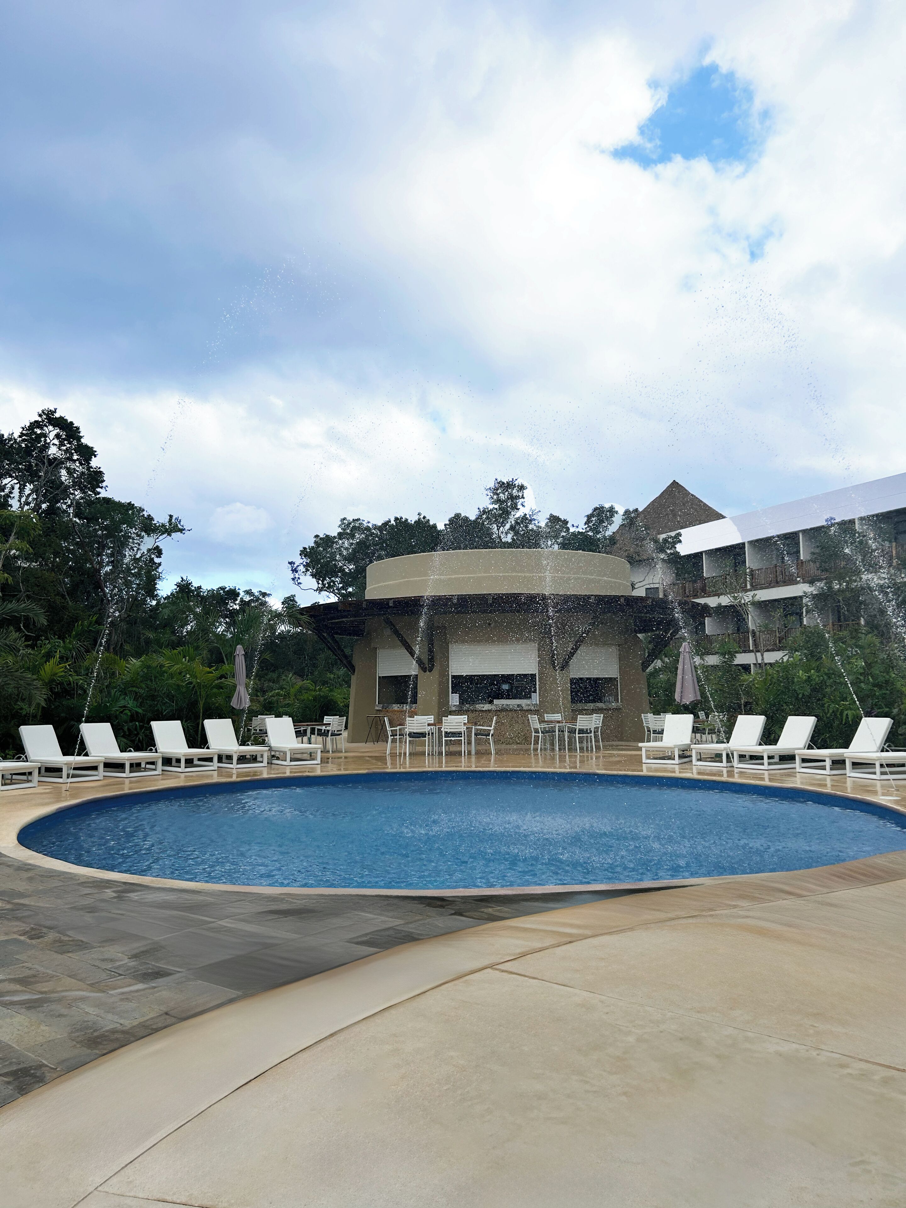 Piscina com espreguiçadeiras e um edifício ao fundo.