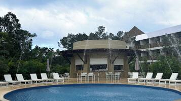 Piscina com espreguiçadeiras e um edifício ao fundo.