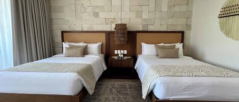 A hotel room with two beds, a stone wall, a wooden headboard, a patterned rug, and a nightstand with a lamp.