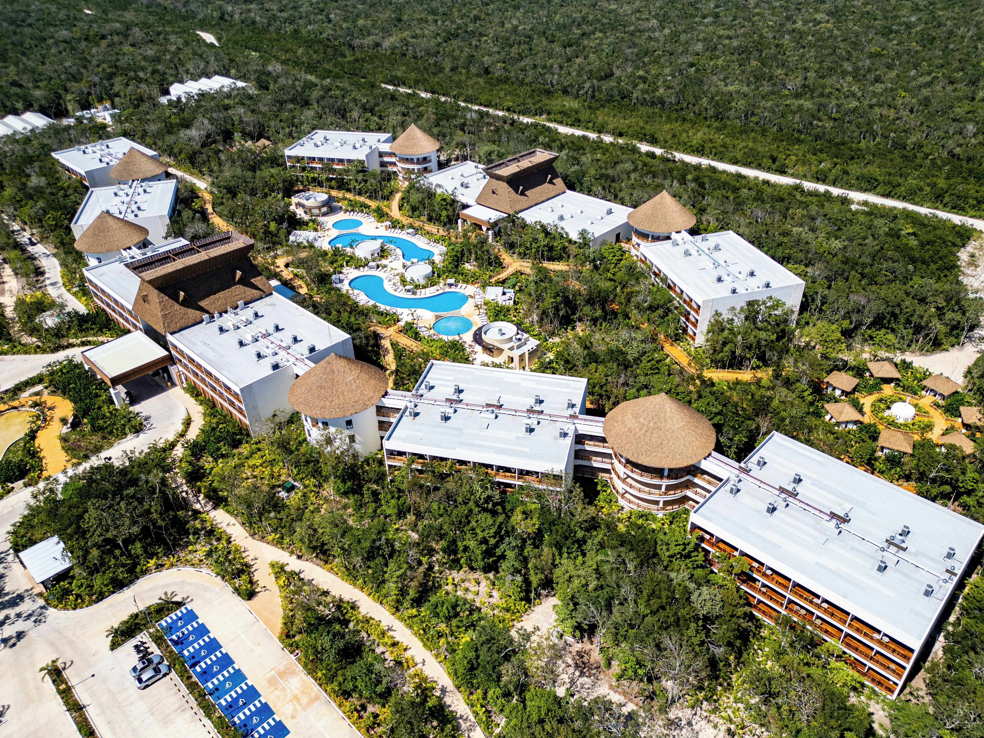 An aerial view of a resort with multiple buildings, swimming pools, and a parking area.