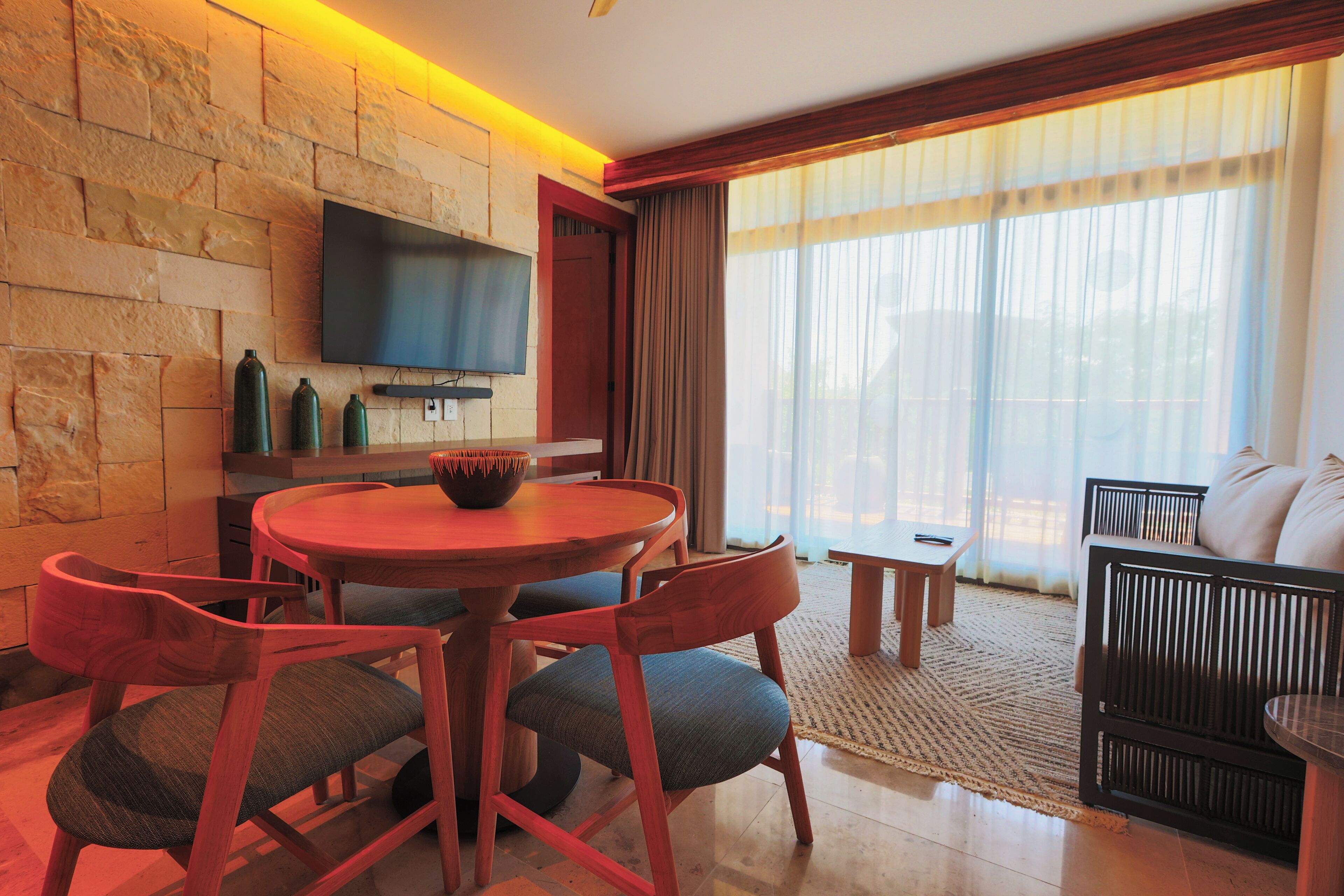 A modern living room with a stone wall, a flat-screen TV, a round wooden table, and a sofa.