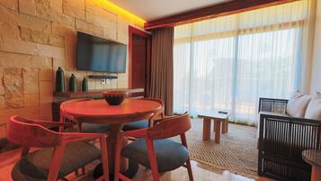 A modern living room with a stone wall, a flat-screen TV, a round wooden table, and a sofa.