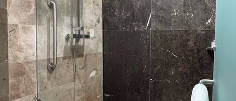 A modern bathroom with a glass-enclosed shower, a wooden bench, and a towel rack.