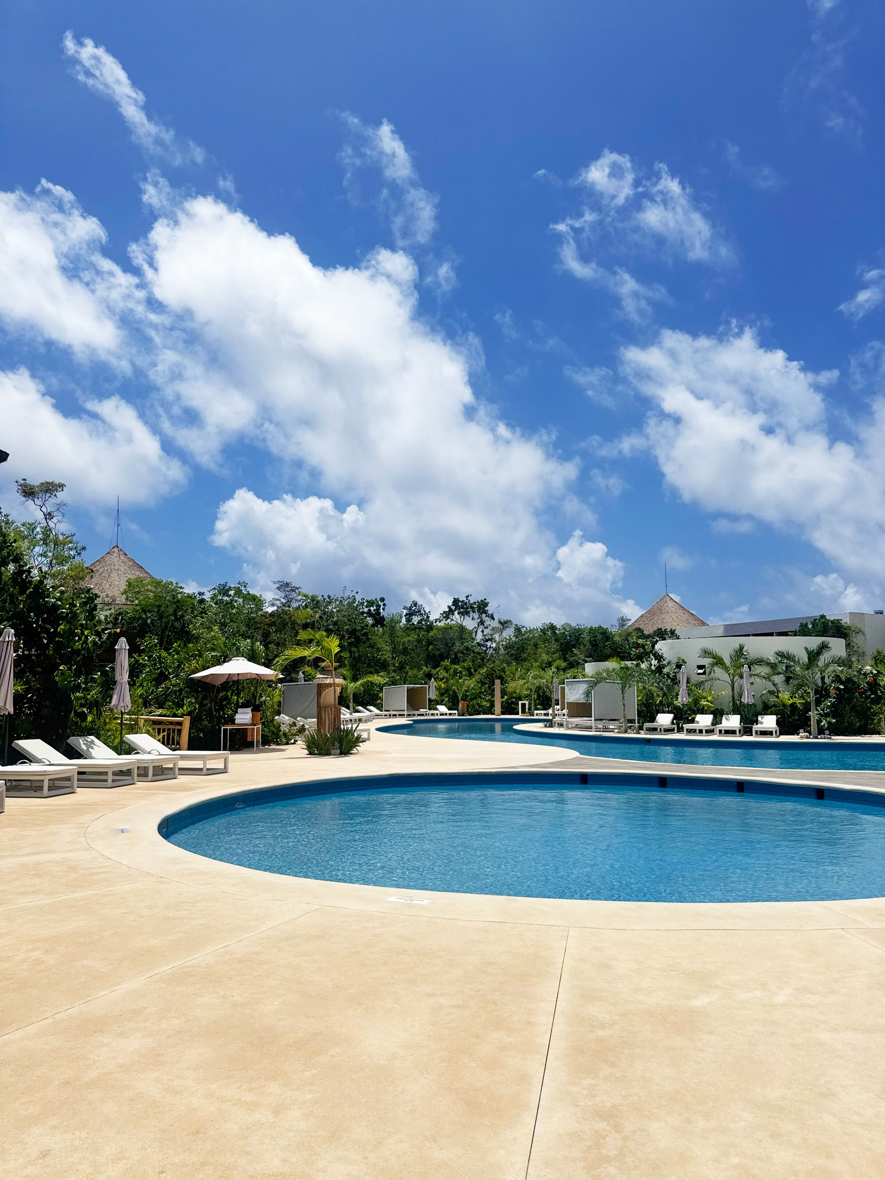 A pool area with lounge chairs and umbrellas, surrounded by greenery and buildings with a modern design.