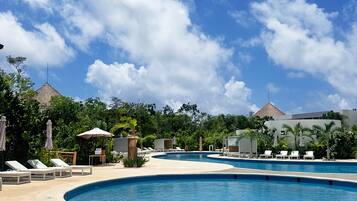 A pool area with lounge chairs and umbrellas, surrounded by greenery and buildings with a modern design.