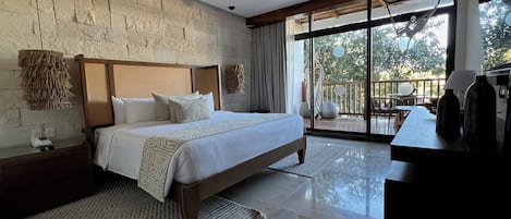Un dormitorio moderno con una cama grande, cabecera de madera, pared de piedra, ventilador de techo y vistas al exterior a través de amplios ventanales.