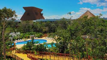 Un resort con piscina, terraza de madera y un gran edificio en forma de pirámide al fondo.