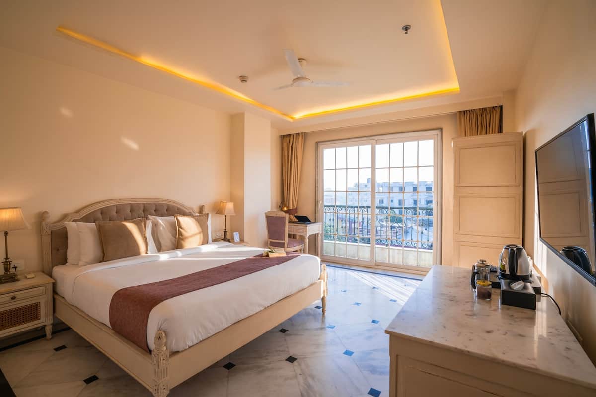 A hotel room with a large bed, a desk with a flat-screen TV, a ceiling fan, and a window with a city view.