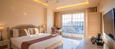 A hotel room with a large bed, a desk with a flat-screen TV, a ceiling fan, and a window with a city view.