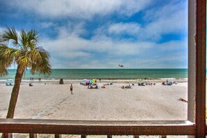 A beach with a palm tree, umbrellas, and a plane in the distance.