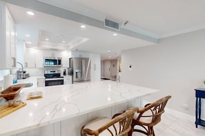 A modern kitchen with white cabinetry, stainless steel appliances, and a large marble island.