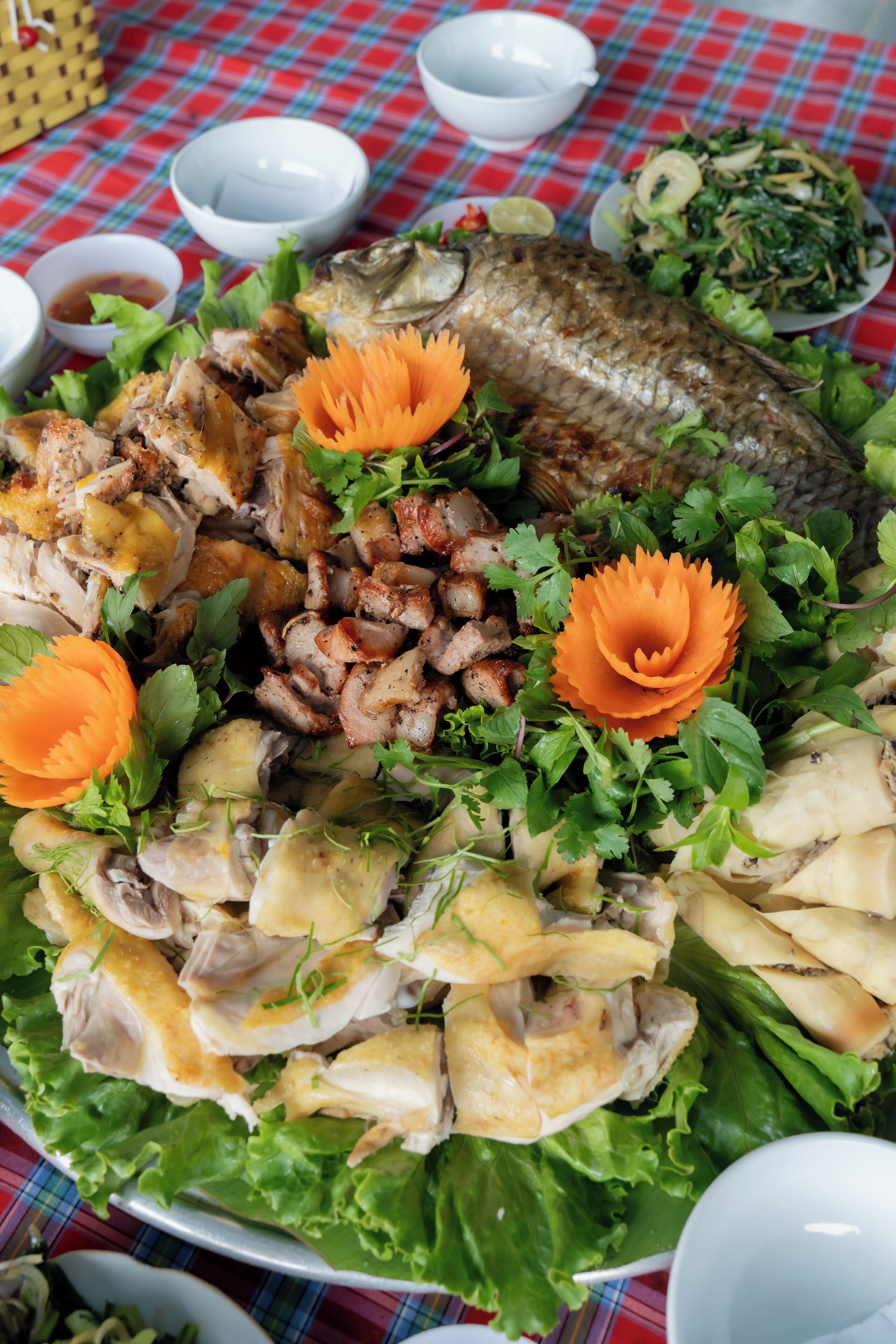Une table sur laquelle sont disposés divers aliments, notamment un poisson entier, des tranches de viande et des légumes, le tout présenté sur une nappe à carreaux.