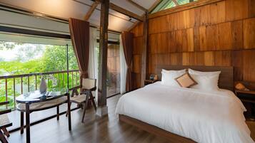Een slaapkamer met een groot bed, houten wanden, een balkon met tafel en stoelen, en uitzicht op groen.
