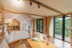 A spacious bedroom with a large bed, a wooden desk, and a view of lush greenery through large windows. - Gia Trang Heian Hoa Binh (Hoa Binh)