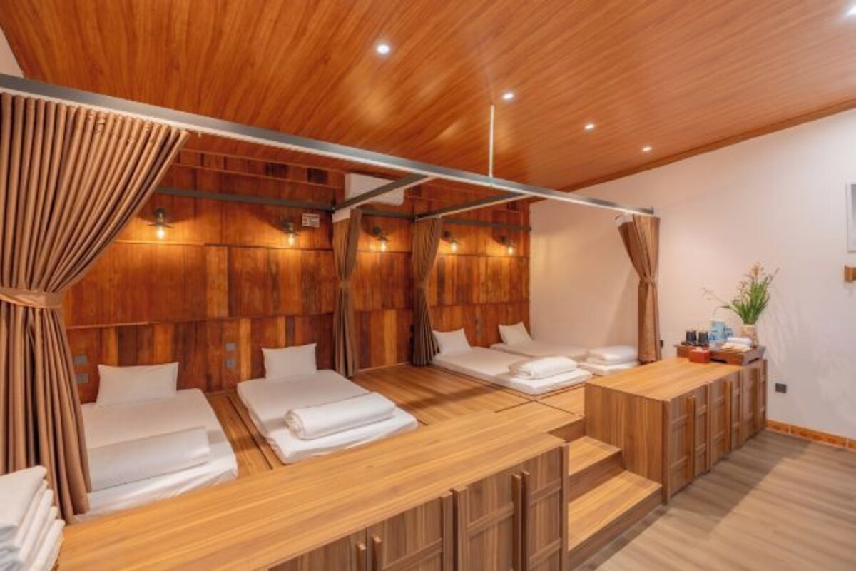 Una habitación con paneles de madera, dos camas, un escritorio de madera y una planta pequeña.