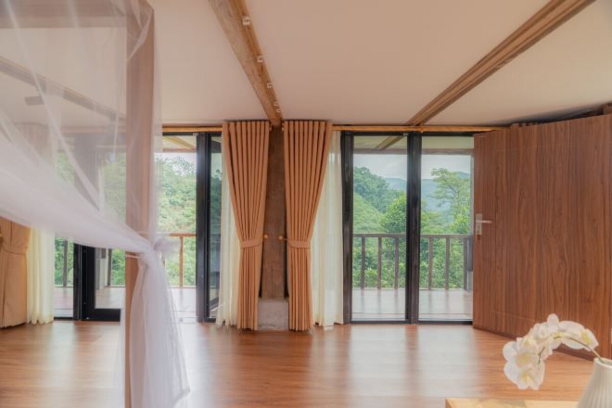 Amplia habitación con ventanas grandes, suelo de madera y vistas al exterior.