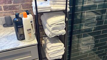 Ein Badezimmer mit gefliestem Duschbereich, einem Handtuchhalter mit gefalteten Handtüchern und Pflegeprodukten auf einer Ablagefläche.