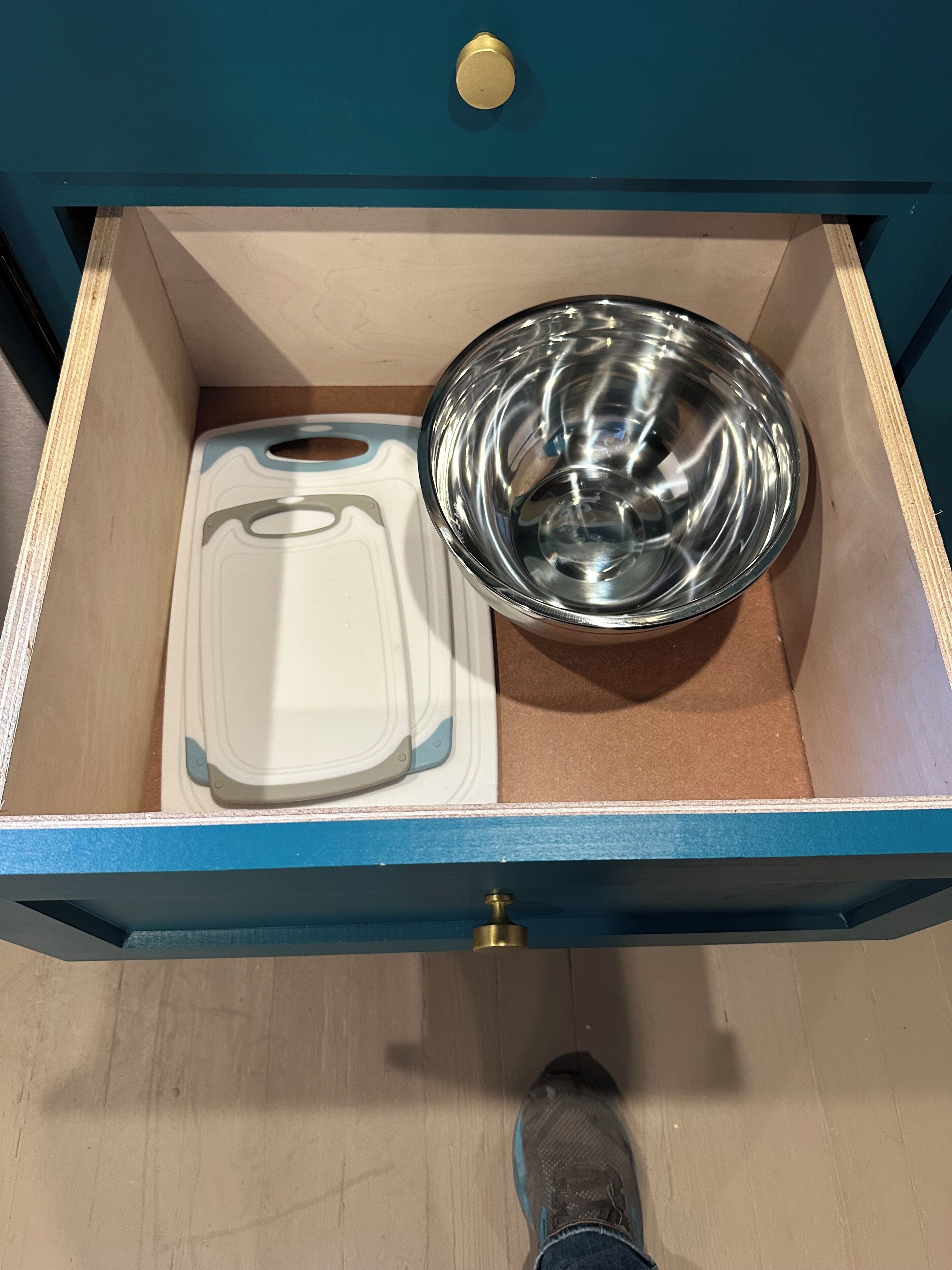 A drawer with a white cutting board and a stainless steel bowl inside.