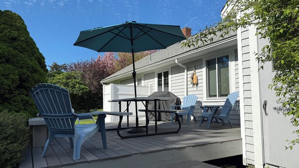 A covered patio with a table and chairs, a grill, and a hanging swing chair. - Orleans Beach Retreat (Orleans)