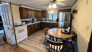 A kitchen with wooden cabinets, a white stove, a microwave, a refrigerator, and a dining table with chairs. - Orleans Beach Retreat (Orleans)