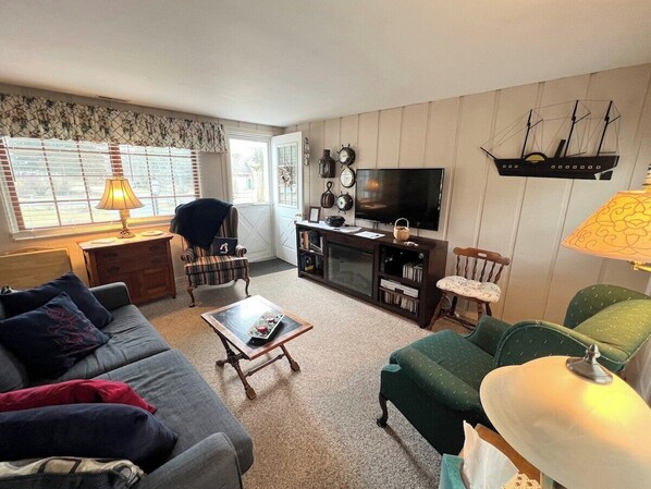 A living room with a sofa, armchair, coffee table, and a TV stand with decorative items.