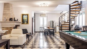 Un vaste salon doté d’un sol à carreaux, d’une table de billard, d’une cheminée et d’un escalier.