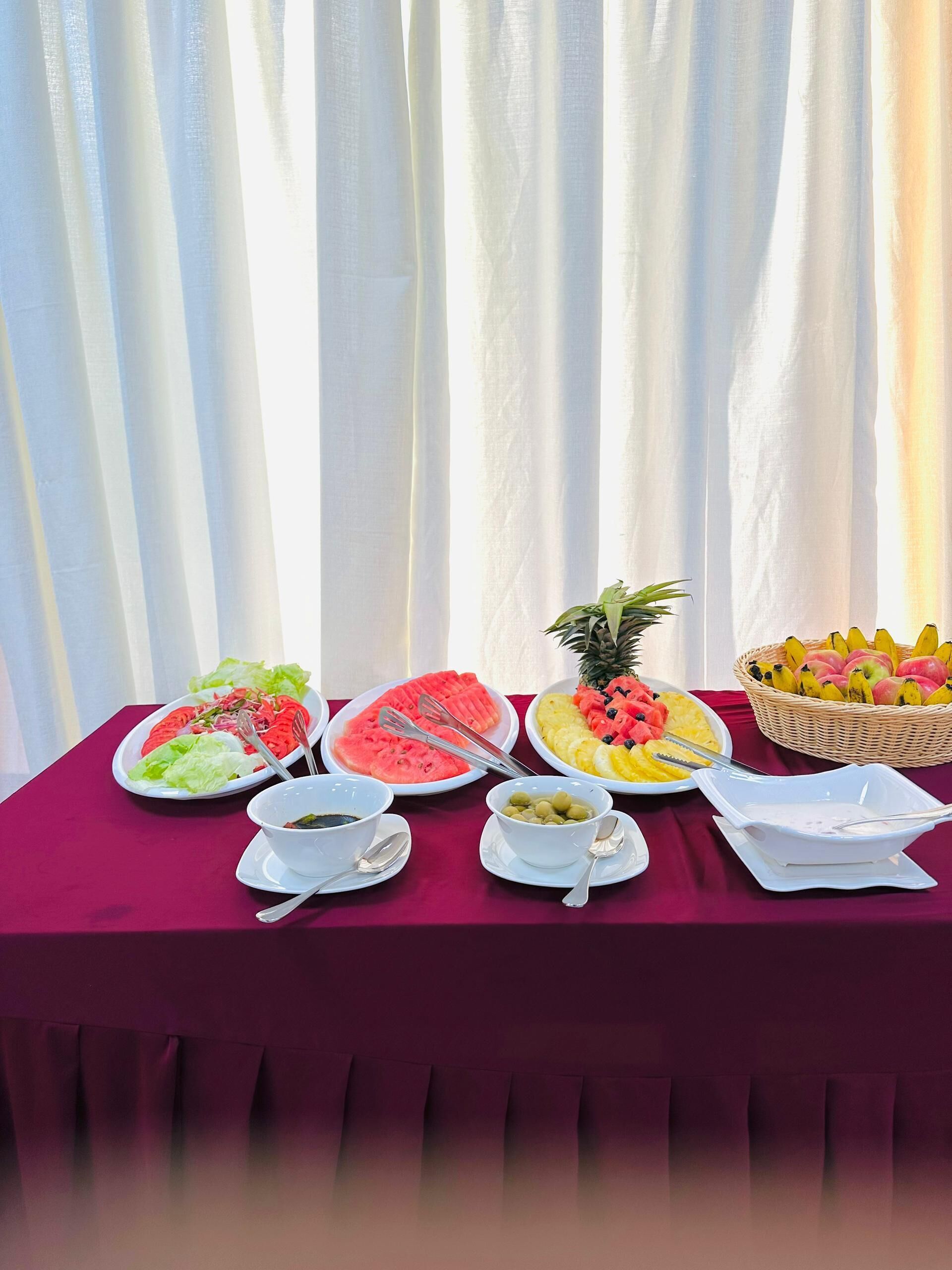 Une table de buffet proposant divers plats, notamment des salades, des fruits et un saladier d’olives.